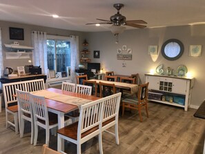 A dining area with a wooden table and white chairs, a ceiling fan, and a window with curtains.
