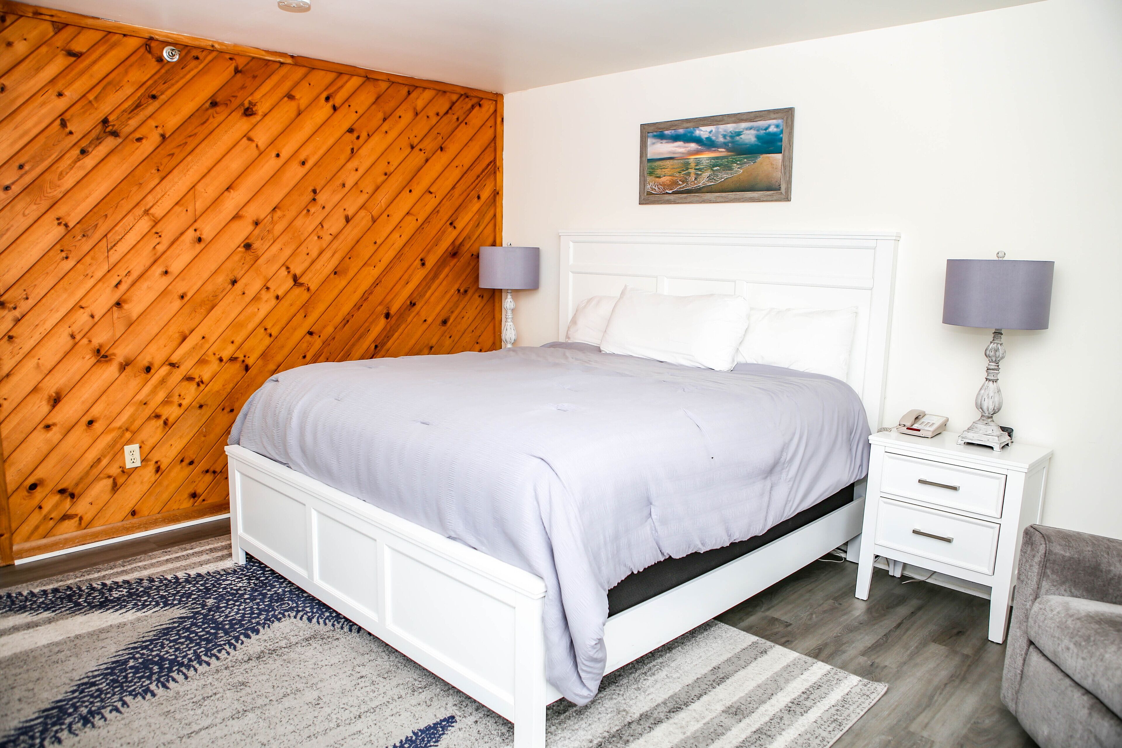 A bedroom with a wooden slat wall, a white bed, two bedside tables with lamps, and a gray sofa.