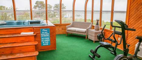 A gym with exercise equipment, a hot tub, and a wicker chair.