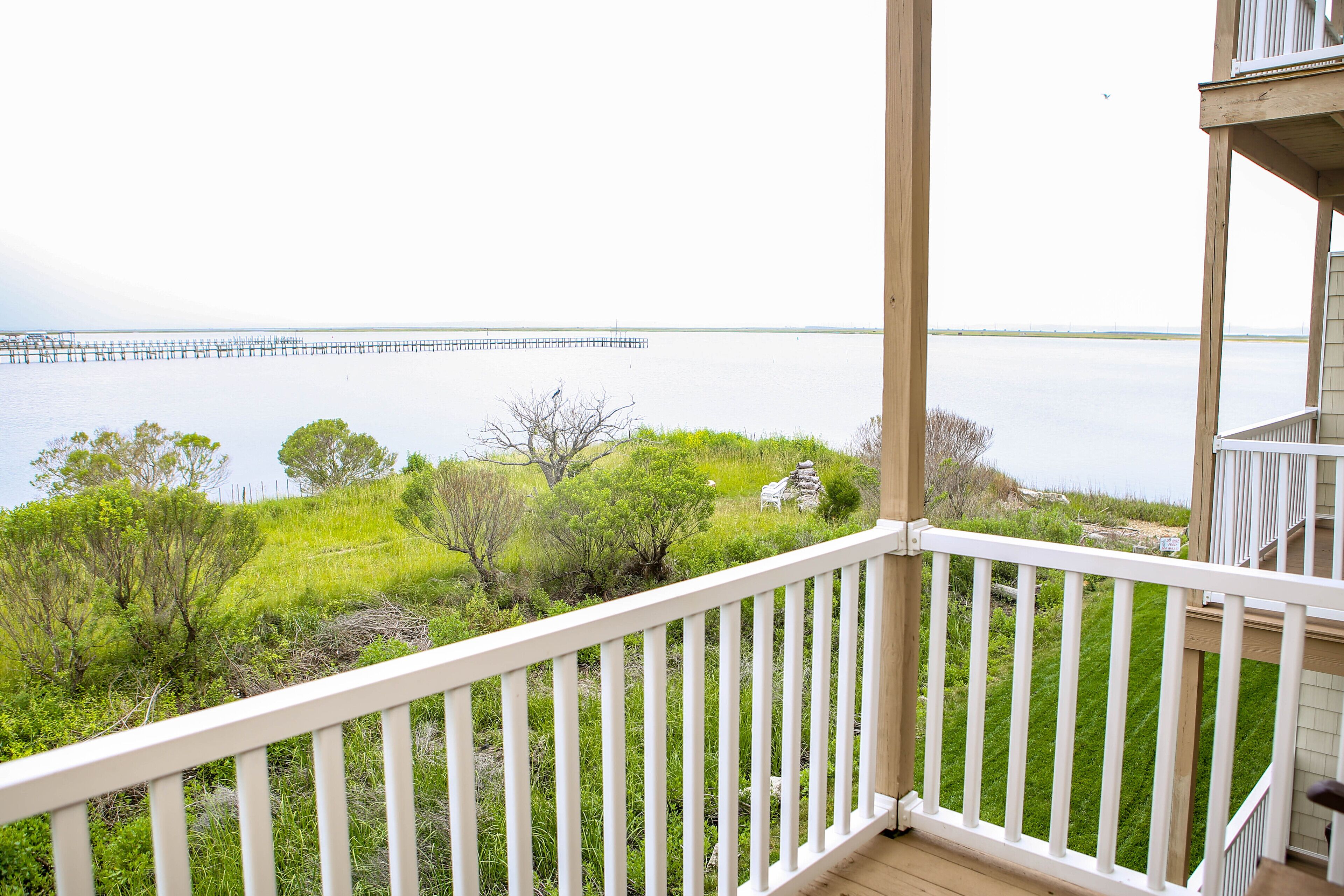 A balcony with a view of a calm body of water and a pier in the distance.