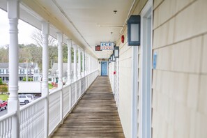 A covered corridor with white columns, a wooden floor, and a sign for 'ICE DRINKS SNACKS'.