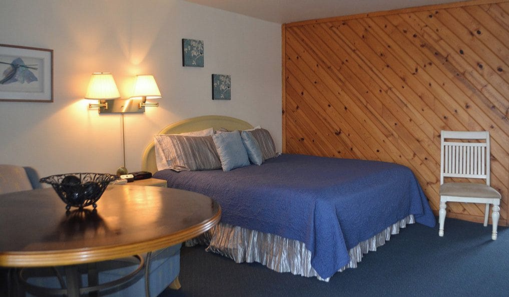 A bedroom with a bed, a chair, a table, and wall-mounted lamps.