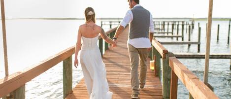 A wooden pier extending over calm water, with a couple walking hand in hand.