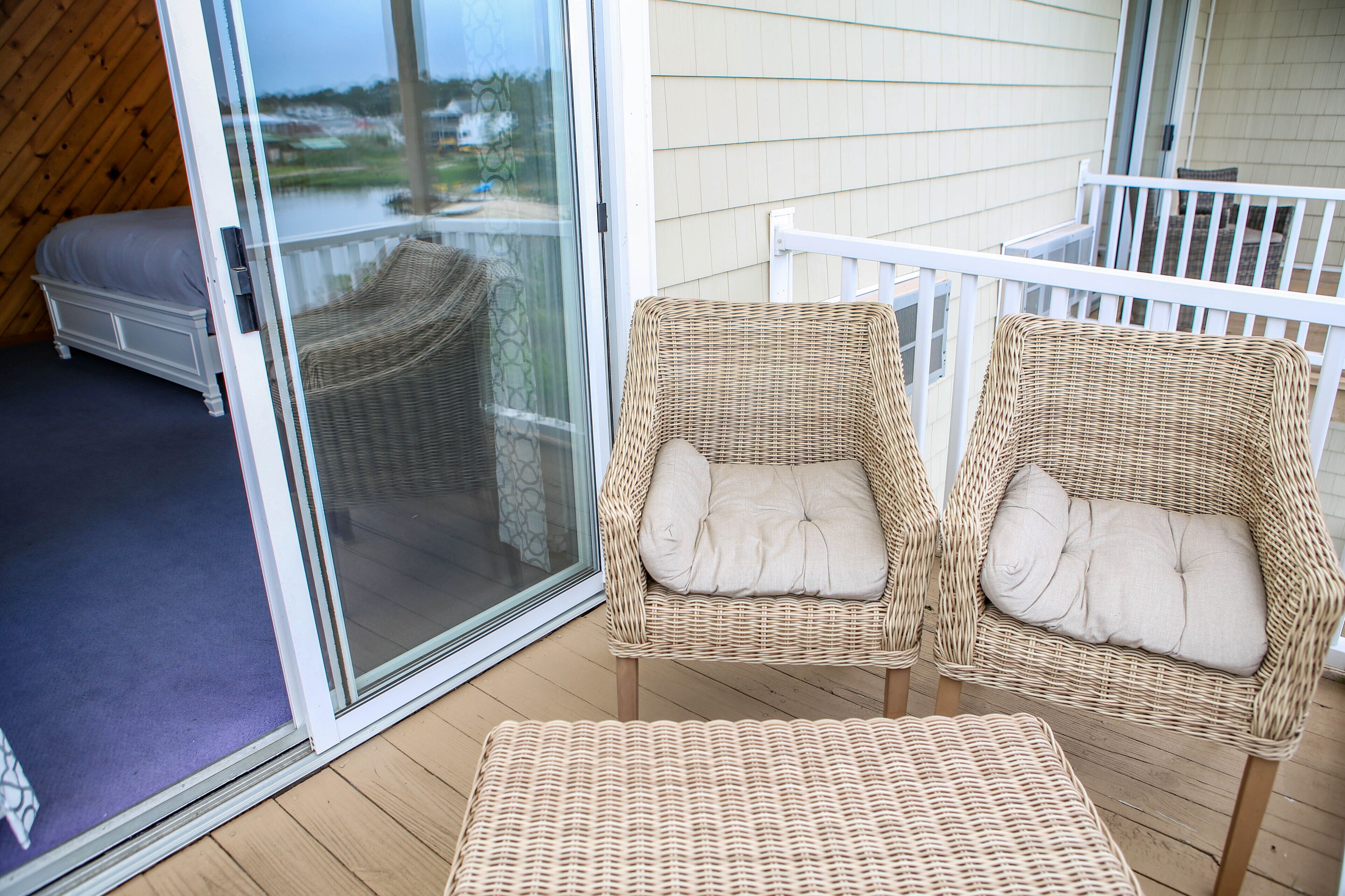 A balcony with wicker chairs and a sofa, a sliding glass door, and a view of a body of water.