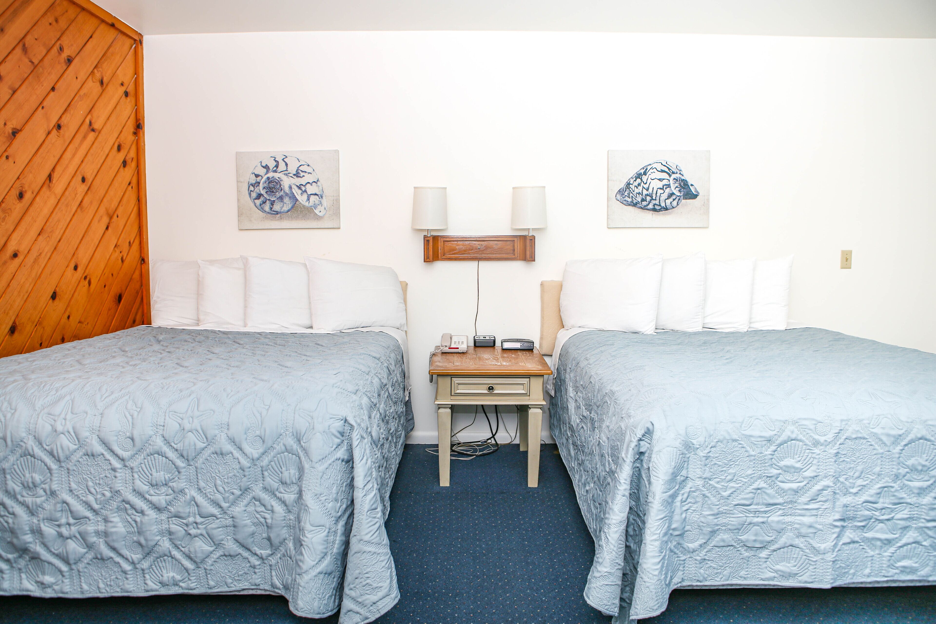 A hotel room with two beds, a wooden wall, and artwork on the walls.