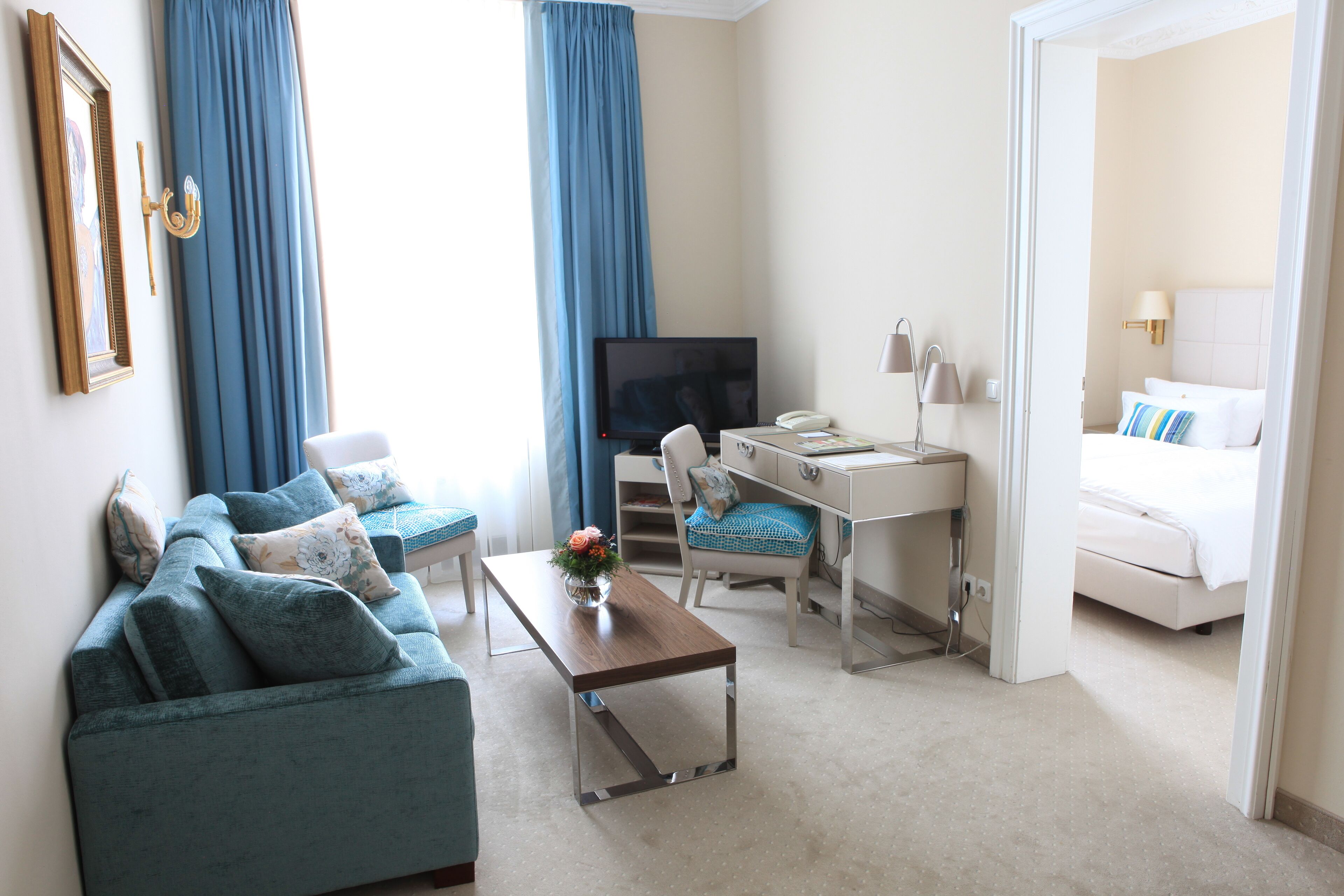 A hotel room with a sofa, a desk, a bed, a TV, and a bathroom visible through an open door.