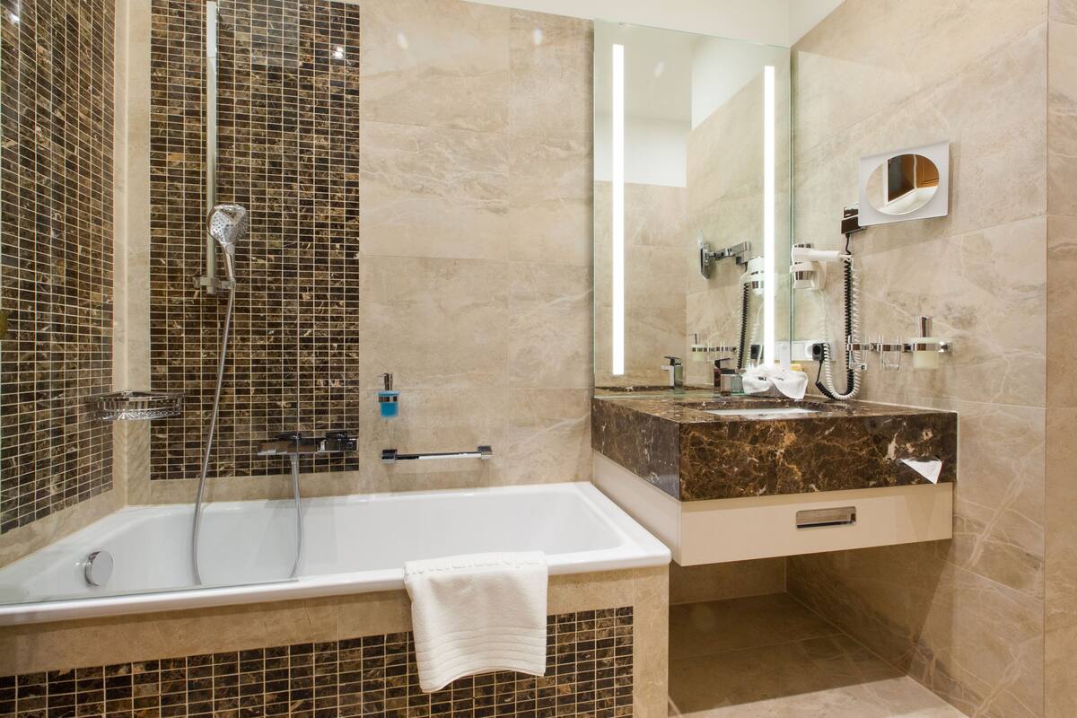 A modern bathroom with a bathtub, a glass-enclosed shower, a vanity with a marble countertop, and a mirror with a built-in light.