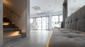 Un moderno vestíbulo de hotel con una imponente escalera, un área de estar confortable y amplias puertas de cristal que dan al exterior.