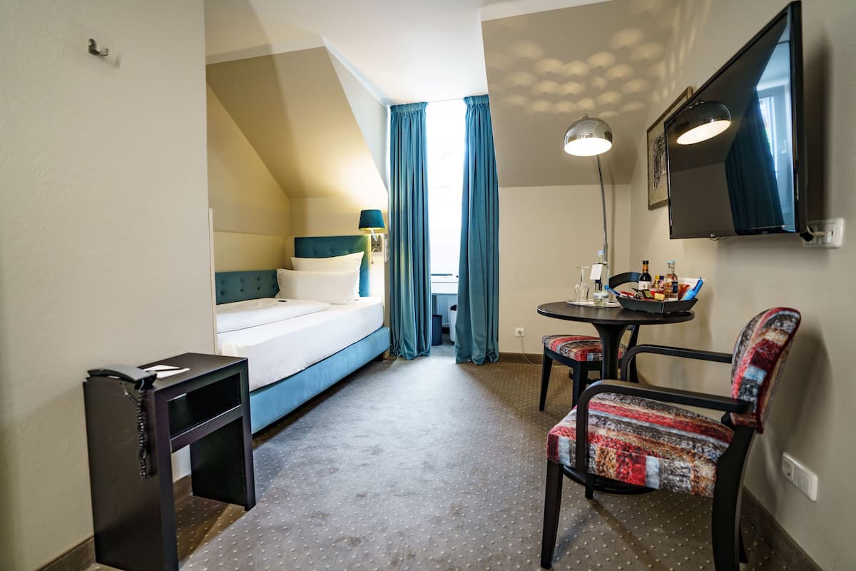 A compact hotel room with a bed, a desk, a chair, and a TV.