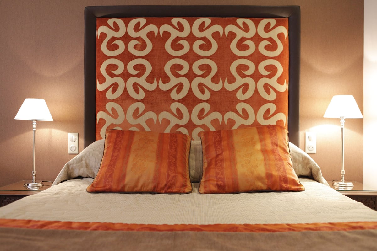 A neatly made bed with two pillows, a patterned headboard, and two bedside lamps.