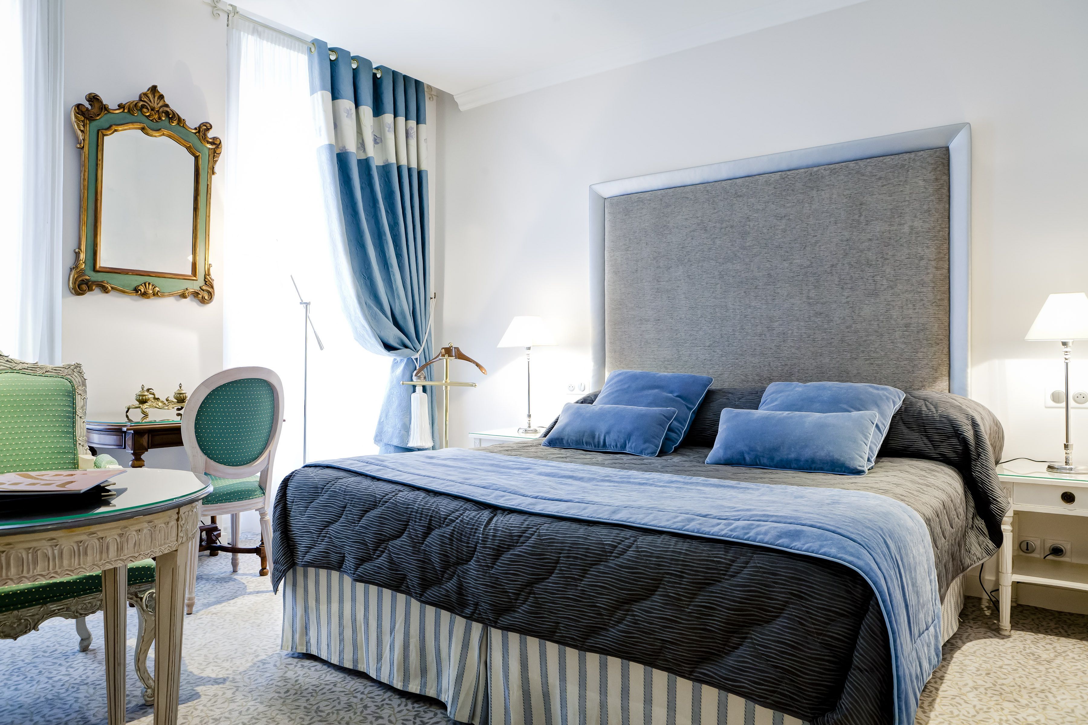 A bedroom with a large bed, a chair, a table, and a mirror.