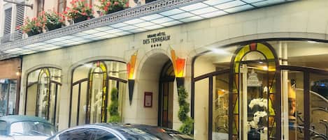 A black car parked in front of the Grand Hotel Des Terreaux, with flower boxes on the balcony and a sign above the entrance.