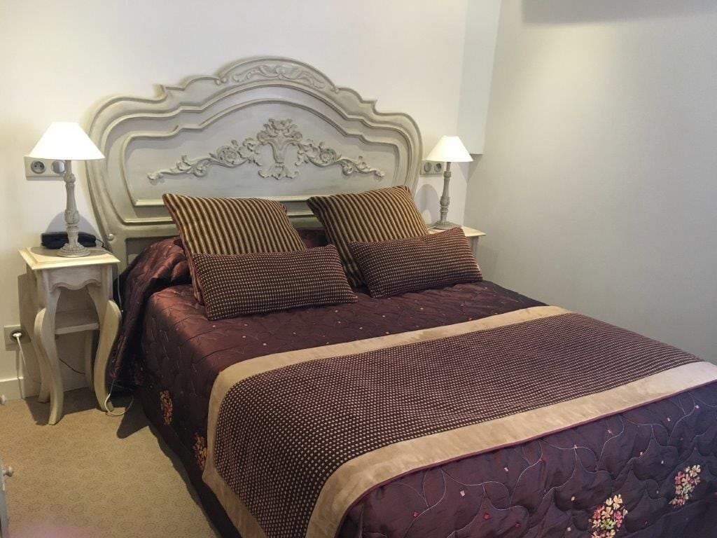 A neatly made bed with a patterned bedspread and pillows, a decorative headboard, and bedside lamps on matching nightstands.