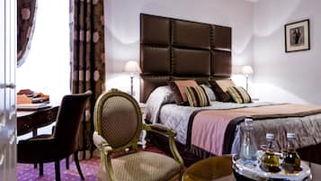 Een hotelkamer met een groot bed, een bureau, een stoel en een nachtkastje met flessen.