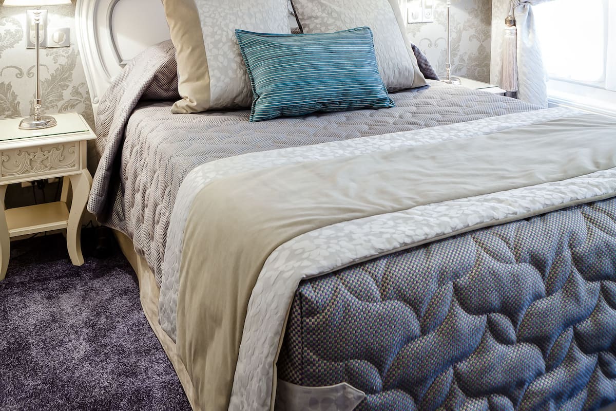 A neatly made bed with a patterned headboard, two bedside lamps, and a window with curtains.