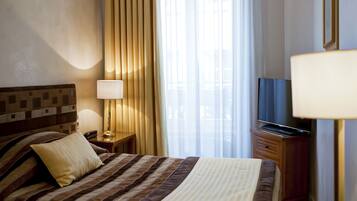 A hotel room with a bed, a bedside table with a lamp, a TV, and a window with curtains.