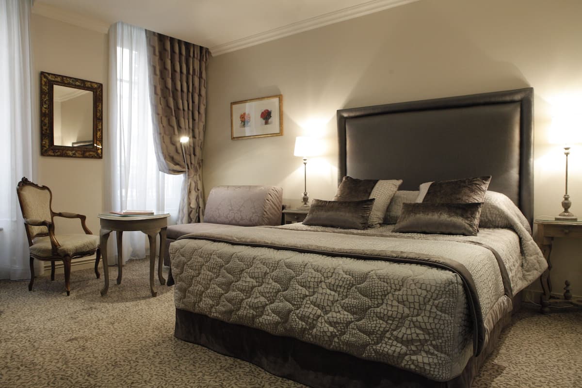 A hotel room with a large bed, a chair, a small table, and a lamp.