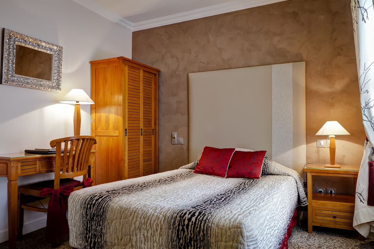 A bedroom with a bed, a desk, a chair, a wardrobe, and two bedside tables with lamps.