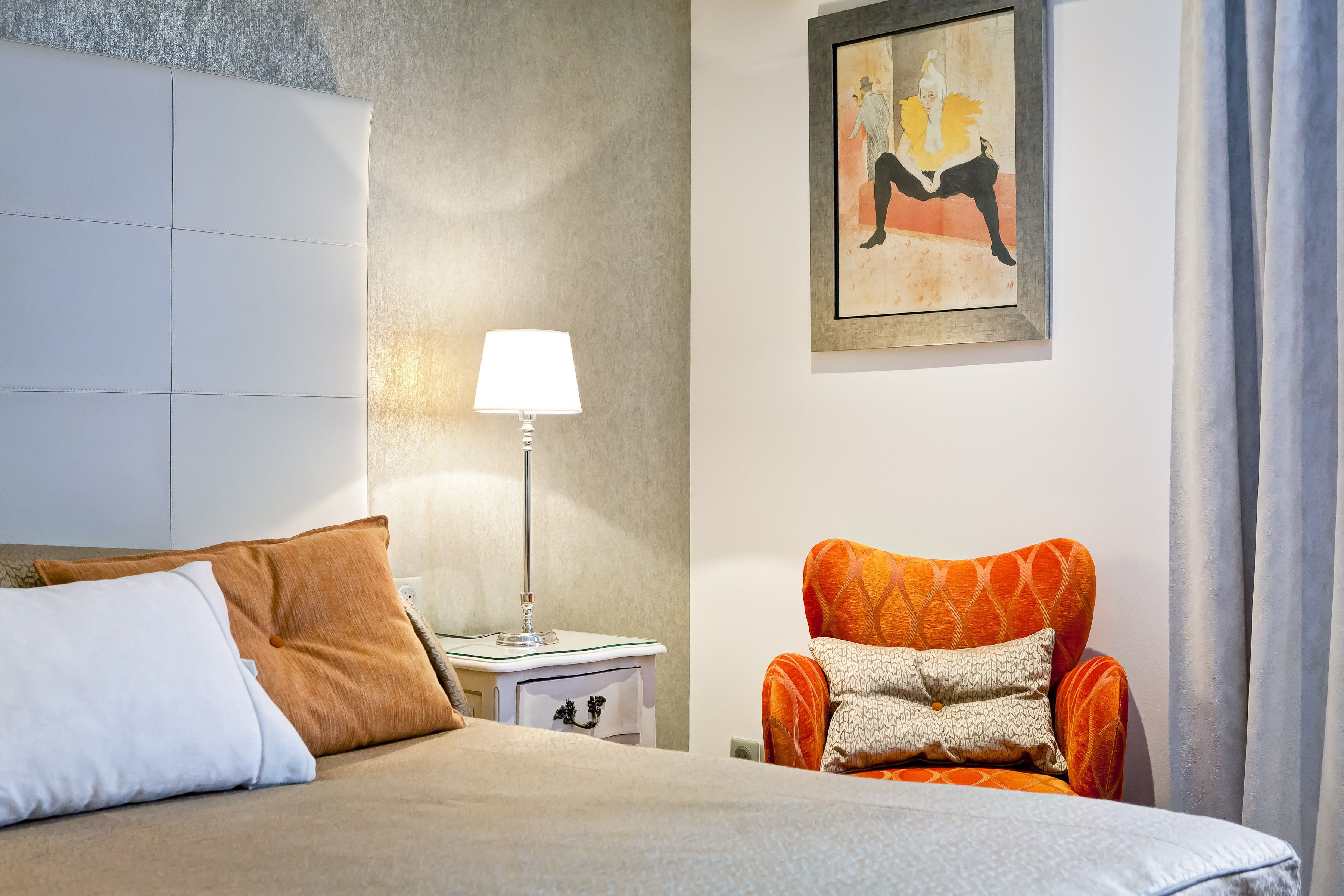 Ein Hotelzimmer mit einem Bett, einem Nachttisch, einer Lampe, einem orangefarbenen Sessel und einem Bild an der Wand.