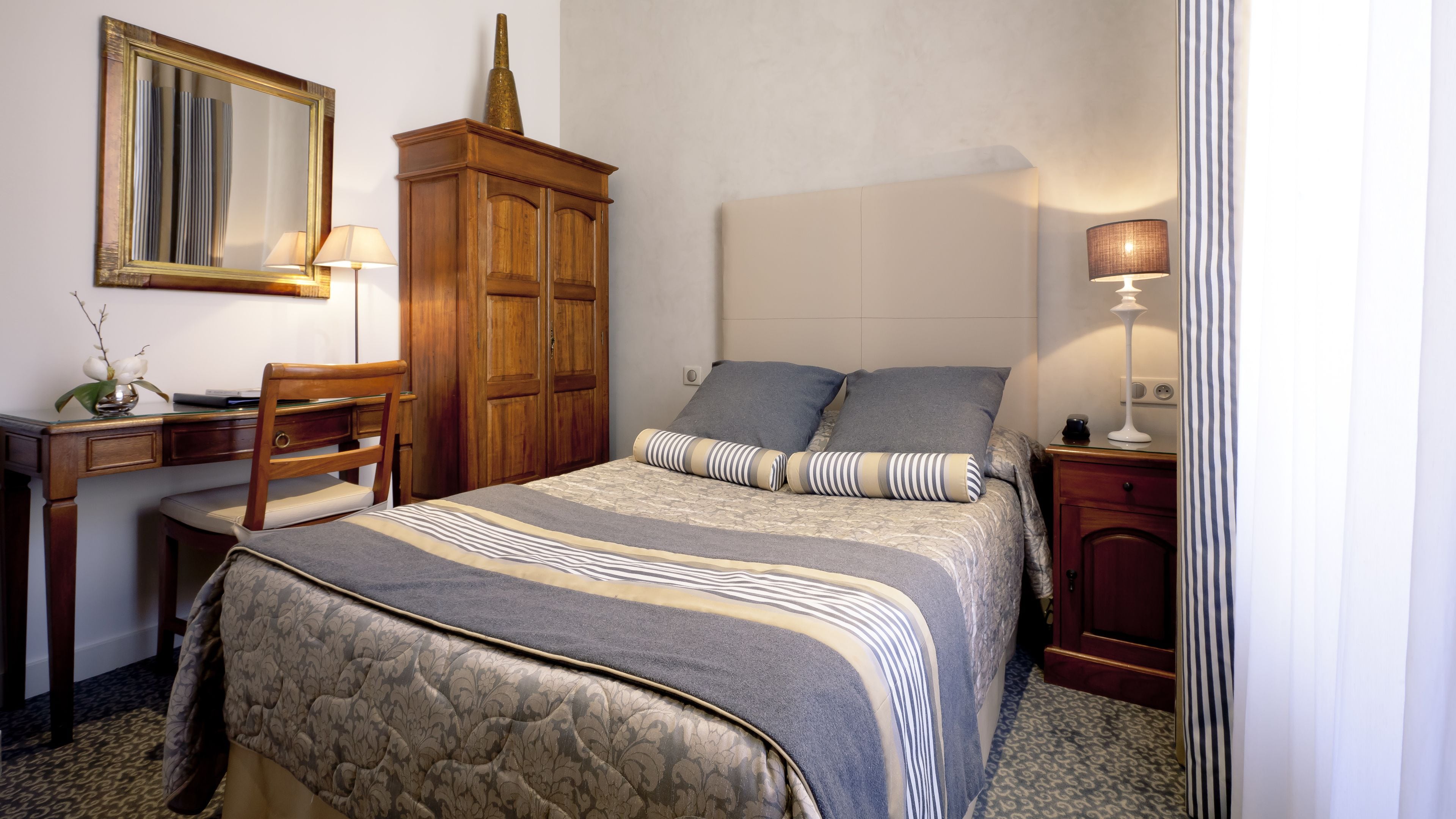 Une chambre à coucher comprenant un lit, un bureau, une chaise, une armoire et une table de chevet avec une lampe.