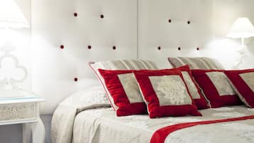 Una cama bien hecha con almohadas rojas y beige, un cabecero blanco con botoneras y una mesita de noche blanca con una lámpara.