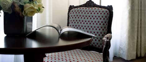 A room with a patterned armchair, a table with a vase of flowers, and a lamp.