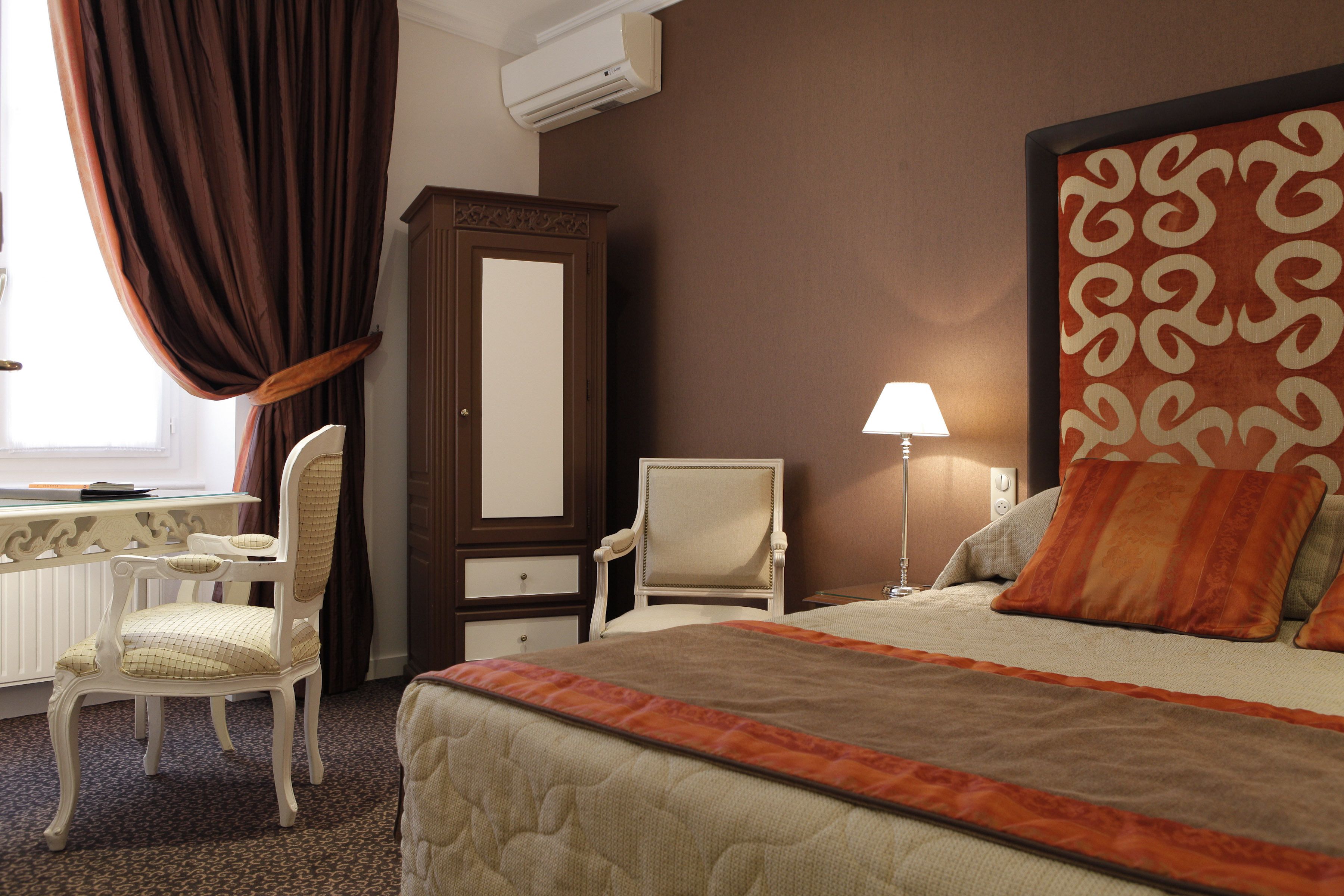 A hotel room with a bed, a desk, a chair, a wardrobe, and a lamp.