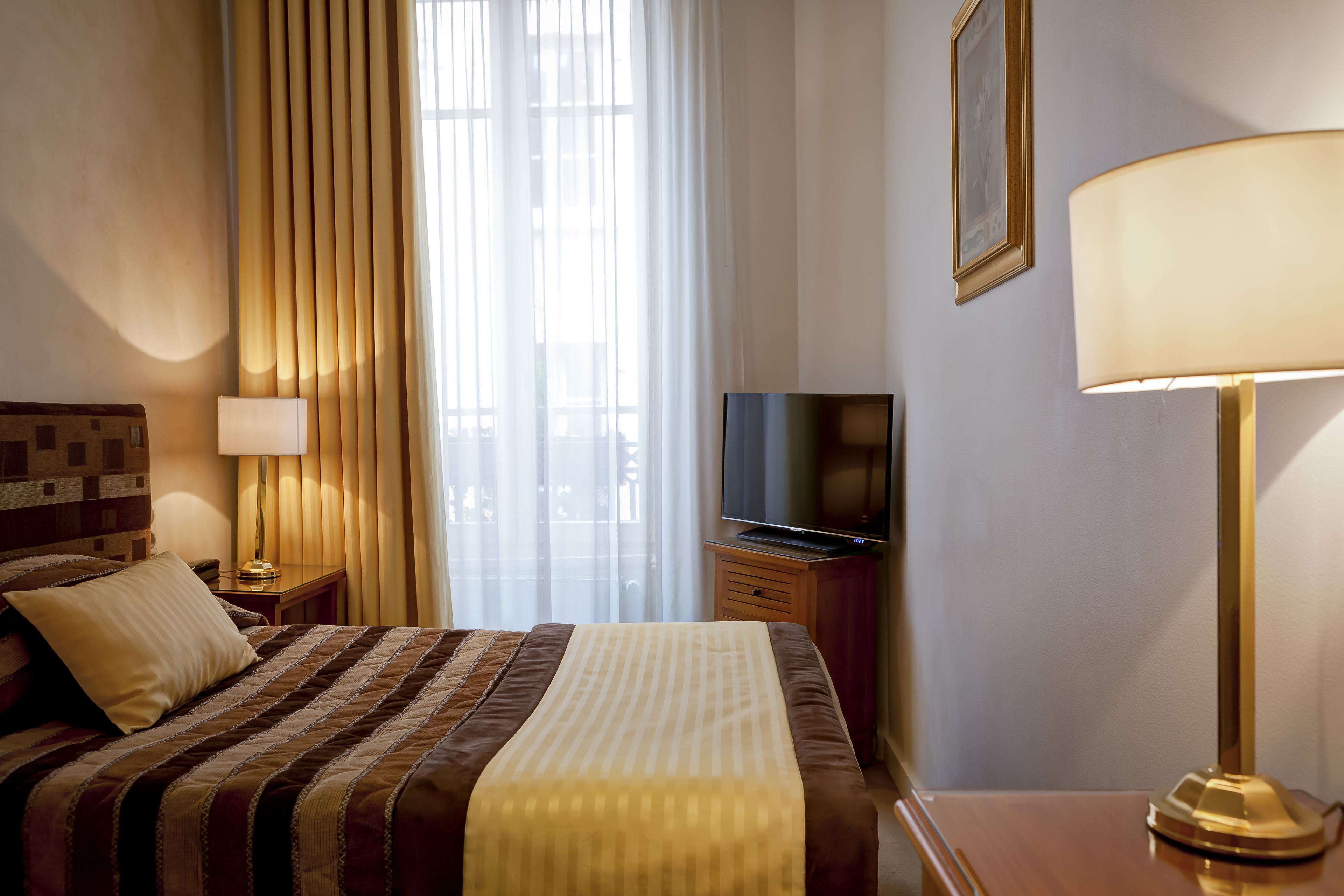 A hotel room with a bed, a television, a lamp, and a window with curtains.