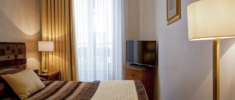 A hotel room with a bed, a television, a lamp, and a window with curtains.