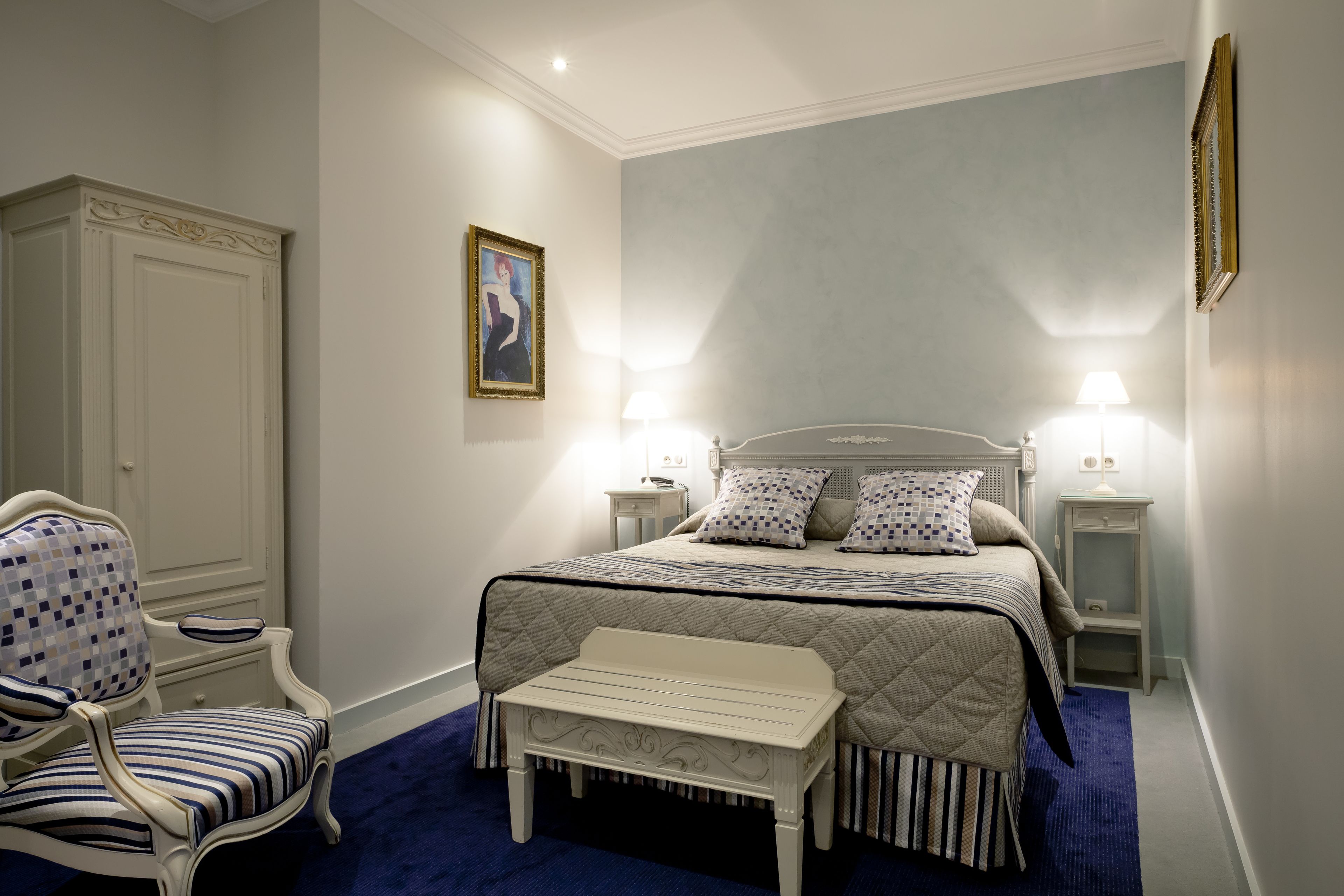 Un dormitorio con cama, mesitas de noche, una silla y un banco.