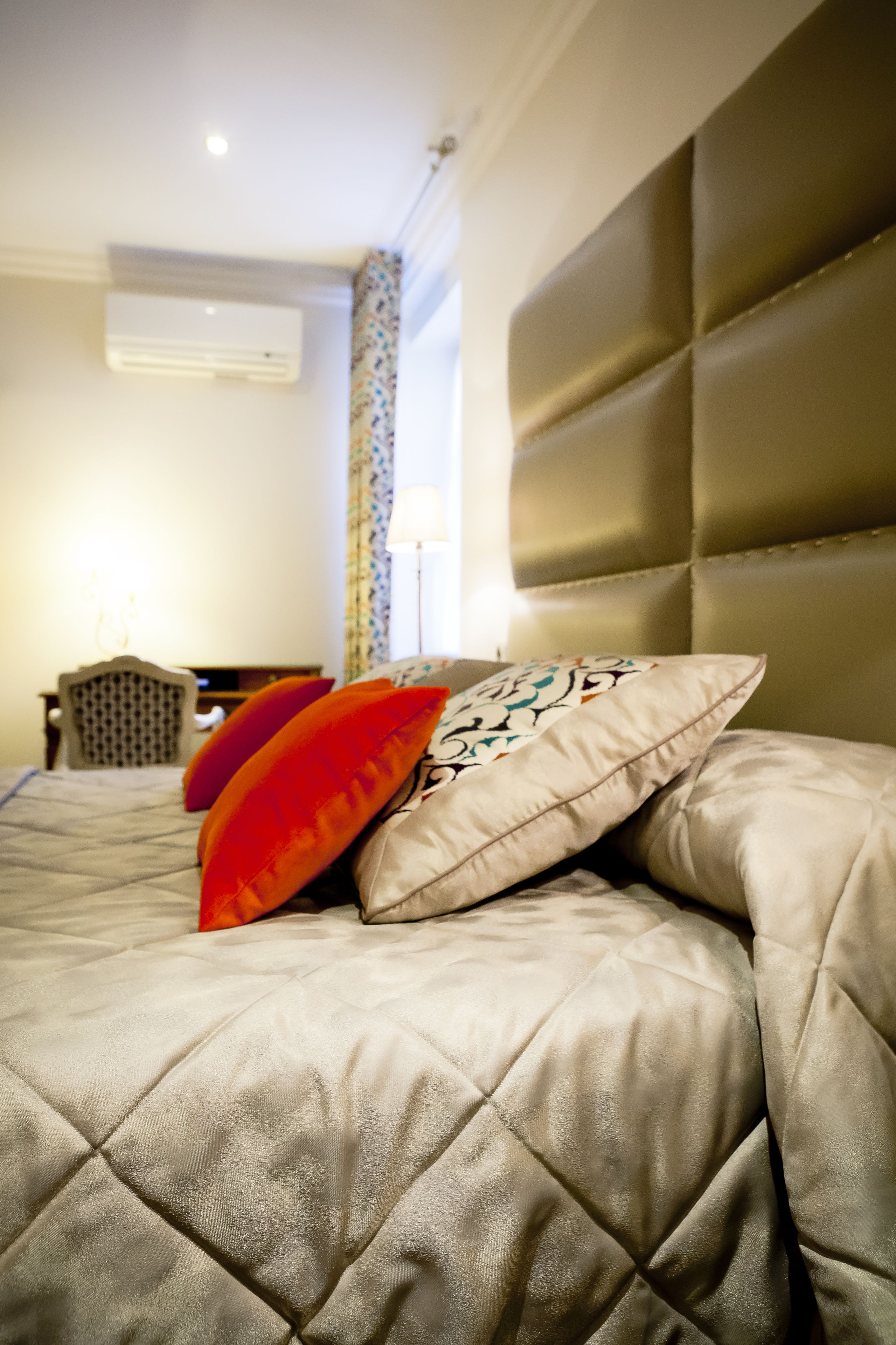 A bed with a quilted headboard, a patterned pillow, and a red pillow.