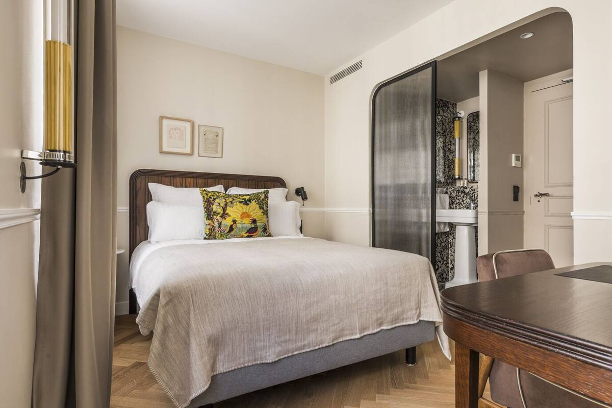 A hotel room with a bed, a wooden table, and a bathroom with a shower and toilet.