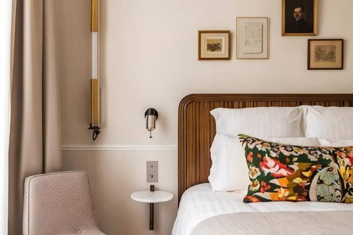 A hotel room with a bed, a chair, a small table, and wall-mounted artwork.
