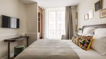 A hotel room with a bed, a TV mounted on the wall, a bedside table, and a window with curtains.