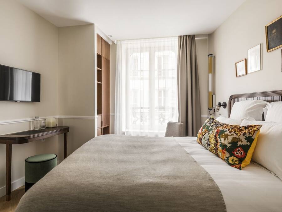 Hotellihuone, jossa on sänky, seinälle asennettu televisio, yöpöytä ja ikkuna, jossa on verhot.
