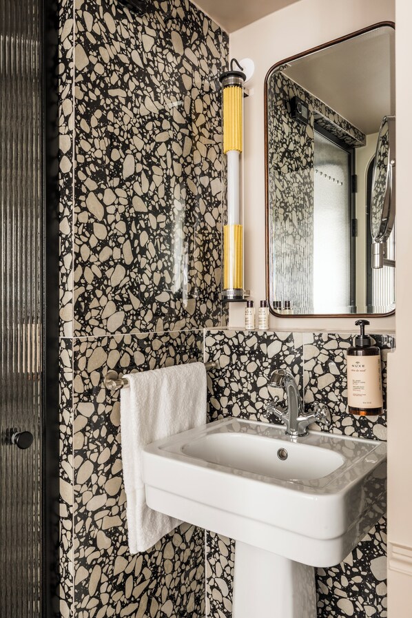 A bathroom with a white sink, a mirror, and a towel hanging on the wall. - Hôtel Chamar (Paris)