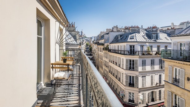 A balcony with a view of Parisian buildings, a table with chairs, and a potted plant. - Hôtel Chamar (Paris)