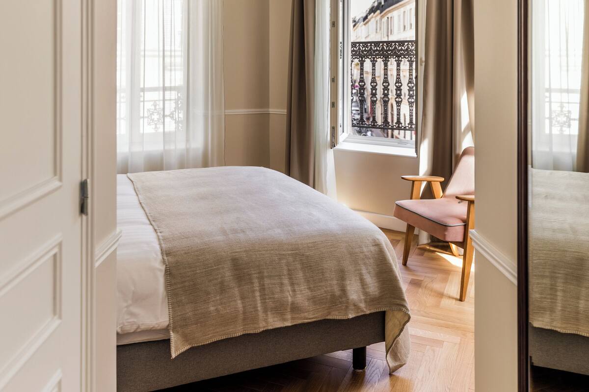 A bedroom with a bed, a chair, and a window with a view of buildings.