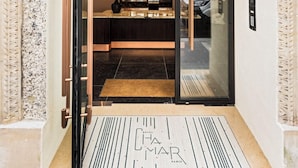A hotel entrance with a glass door, a black mat with text, and a bookshelf visible inside. - Hôtel Chamar (Paris)