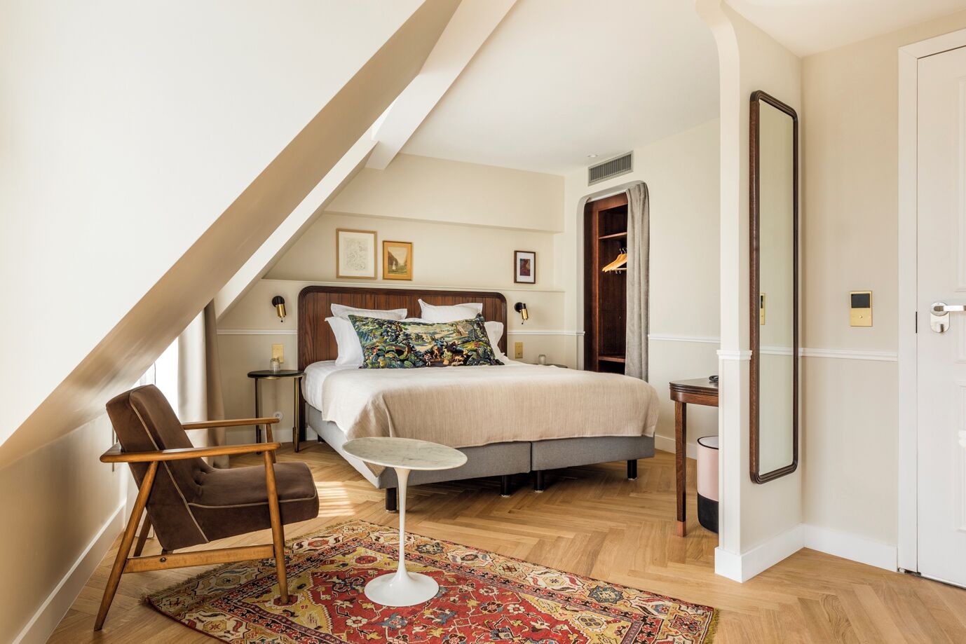 A bedroom with a bed, a chair, a small table, a mirror, and a wardrobe.