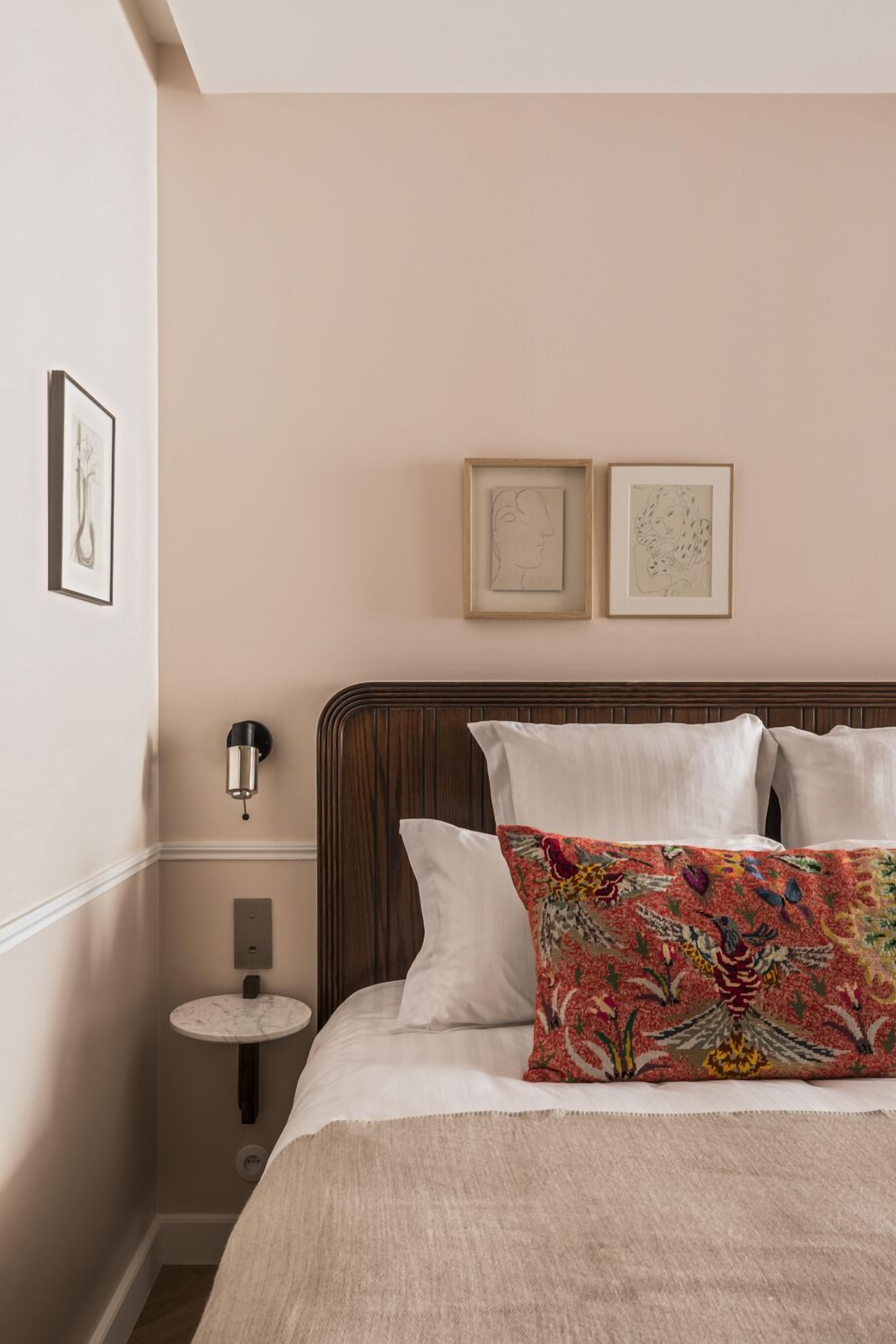 Una cama bien hecha con un cojín estampado, una mesita de noche con una lámpara y cuadros en la pared.