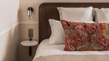 Una cama bien hecha con un cojín estampado, una mesita de noche con una lámpara y cuadros en la pared.