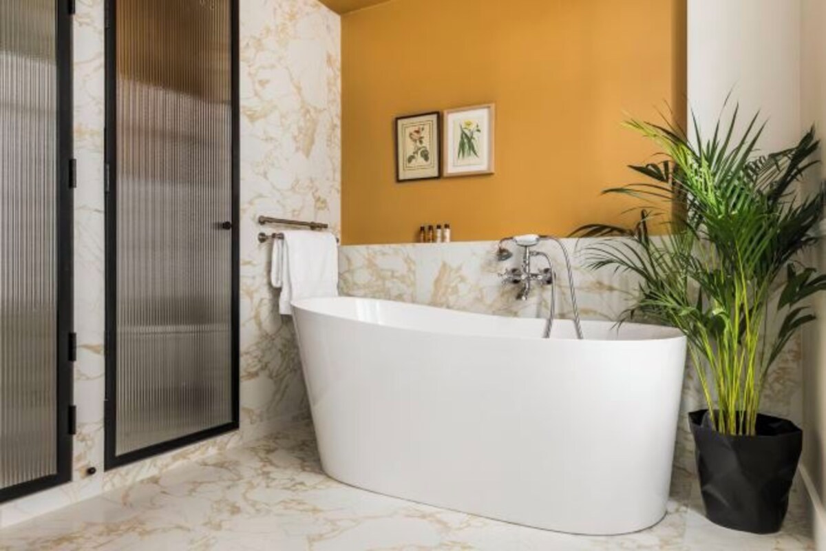 Un baño con una bañera independiente, cabina de ducha, planta en maceta y dos cuadros en la pared.