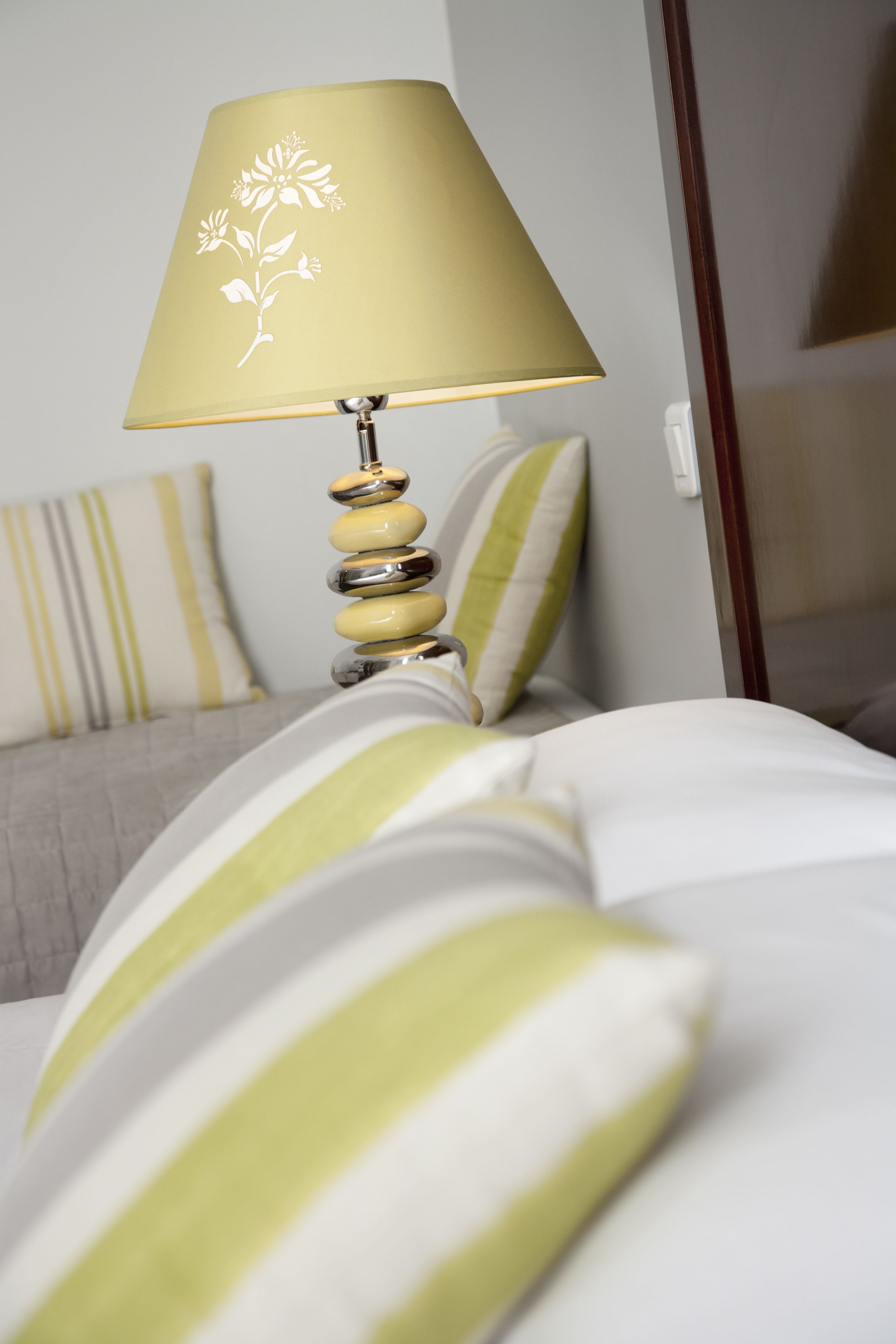 Una cama con almohadas a rayas y una lámpara con motivos florales.