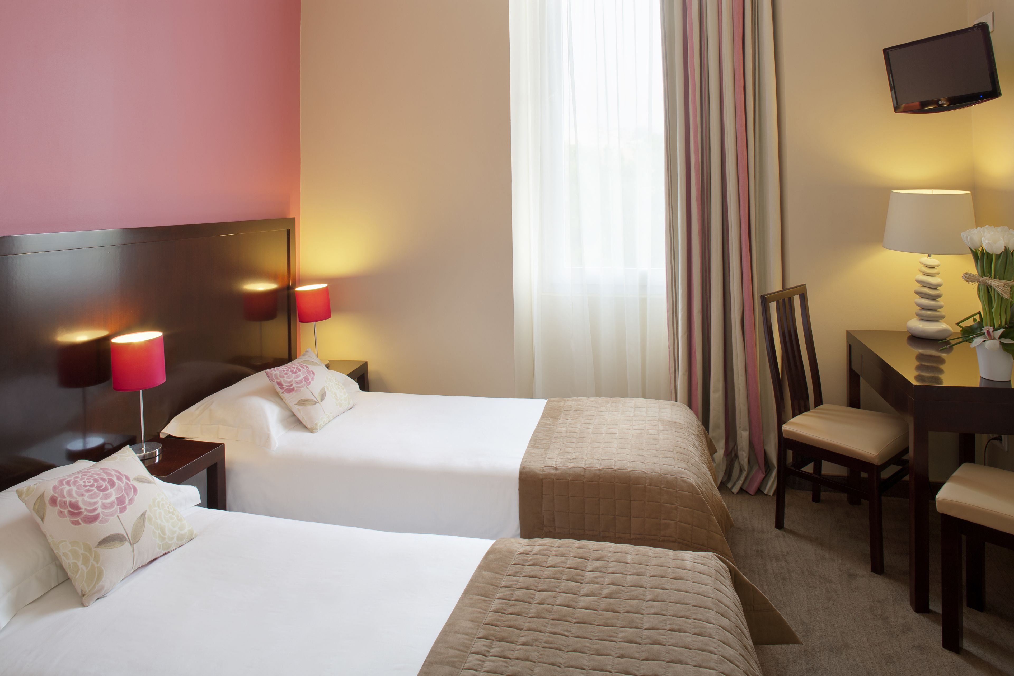 Une chambre d’hôtel avec deux lits, un bureau, une chaise, une télévision et une fenêtre avec des rideaux.
