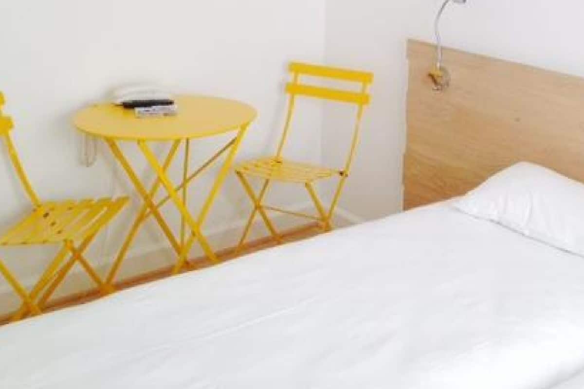 A bed with white bedding, a wooden headboard, and two yellow chairs with a small table.