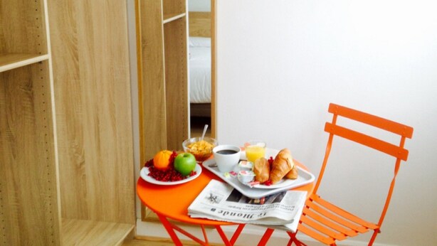 A small room with a wooden wardrobe, a mirror, a table with breakfast items, and a red chair. - Hôtel Opera Dieppe (Paris)