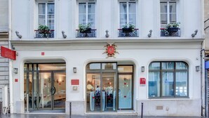 A hotel entrance with glass doors, a coat of arms above the entrance, and potted plants on the windowsills.