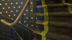 A spiral staircase with a wooden handrail and steps with green and black carpeting.