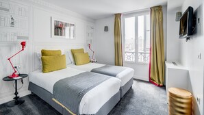 A hotel room with two beds, a desk, a red lamp, a bookshelf, and a window with curtains.
